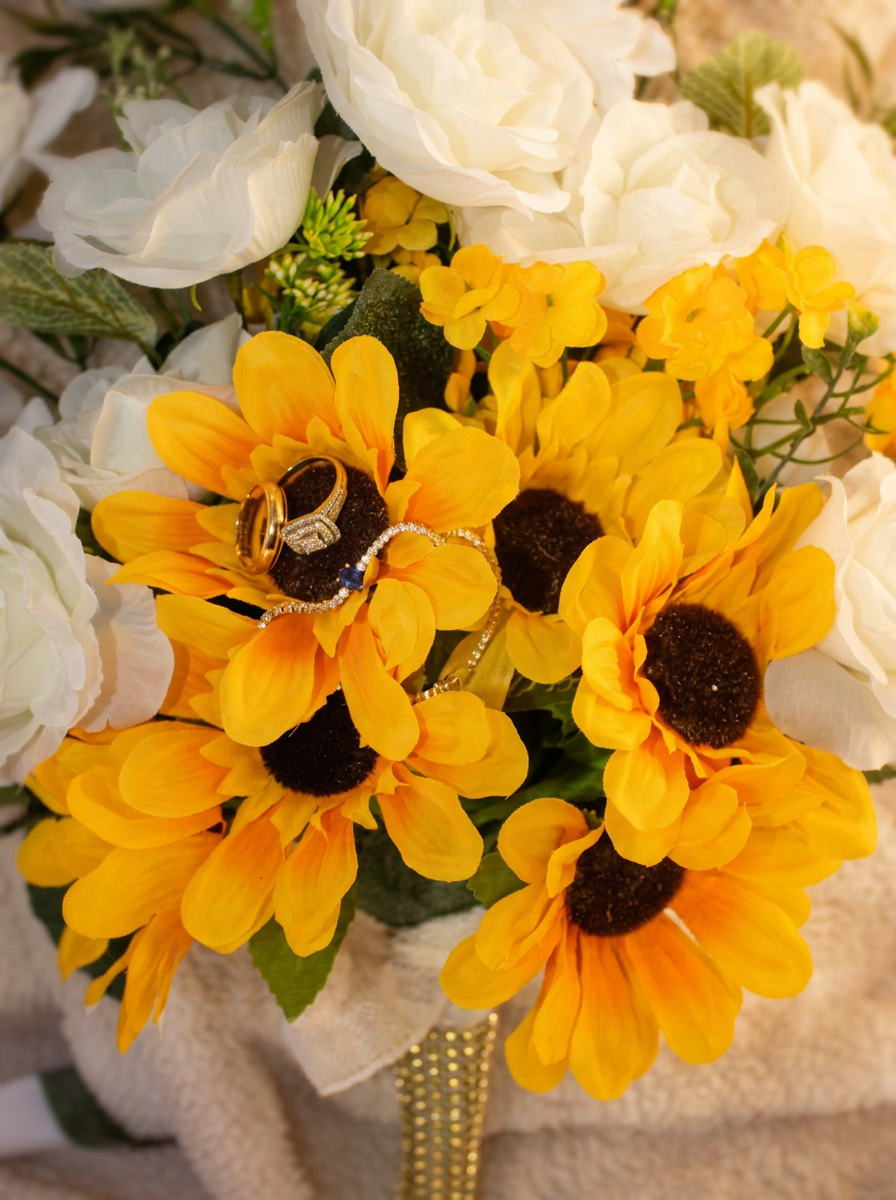 Bridal bouquet of sunflowers and ivory roses with wedding rings and gold jewelry detail